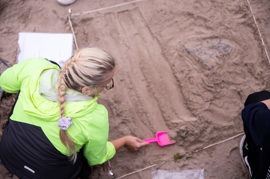 Rantahiekkaan on rajattu narulla neliömetrin kokoinen ruutu, jonka alalta kuvassa etualalla oleva henkilö lapioi hiekkaa tutkimusta varten.